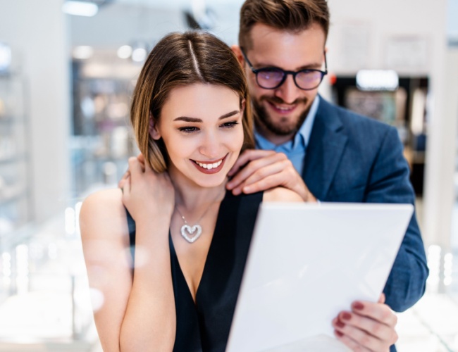 a man and woman standing in a jewelry store together looking at a tablet 