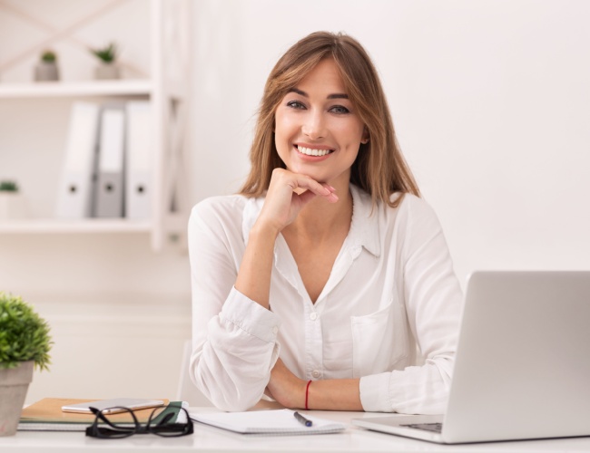 a photograph of an attractive lady sitting at a computer and smiling into the camera