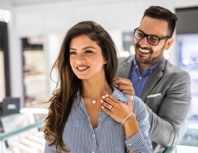 a jeweler helping a lady try on a beautiful necklace